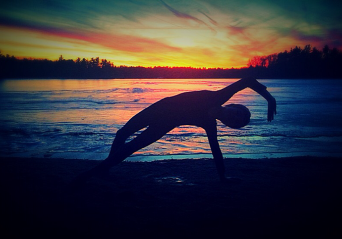 A man doing yoga on the beach at sunset.